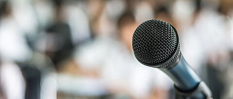 Bild eines Mikrofons mit Publikum im Hintergrund
