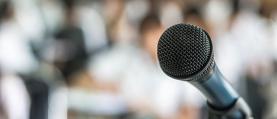 Bild eines Mikrofons mit Publikum im Hintergrund