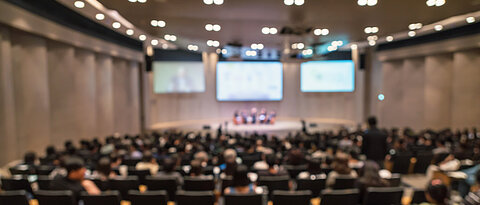 Abstract blurred photo of conference hall or seminar room with speakers on the stage and attendee background