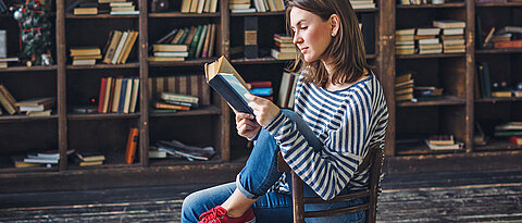 Serious young woman with a book in front of the bookshelves